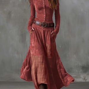 May include: A rust-colored long-sleeve dress with a button-up front, a high collar, and a brown belt. The dress features a flowing skirt with plaid accents and pockets. The model is wearing brown lace-up boots.