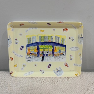 May include: A rectangular cream-colored serving tray featuring a central illustration of a blue storefront labeled "BISTROT du MIDI." The border is decorated with small watercolor-style icons of wine glasses, lobsters, lemon slices, and sailboats.