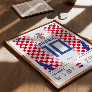 May include: A framed poster featuring a red and white checkered pattern inspired by the Croatian national football jersey. It displays the name MODRIĆ, the number 10, the text LUCA MODRIĆ, player statistics, the HNS crest, and four red stars.