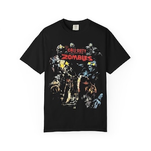 May include: A black short-sleeved t-shirt featuring a graphic print of Call of Duty Black Ops Zombies. The design includes multiple zombie figures with glowing yellow eyes and the red text Call of Duty Black Ops Zombies centred on the chest.