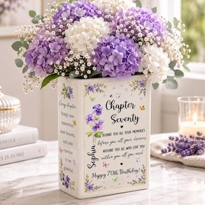 May include: A rectangular white ceramic vase filled with purple and white hydrangea flowers and baby's breath. The vase features floral illustrations, butterflies, and text reading Chapter Seventy, Sophia, and a quote about memories and dreams.