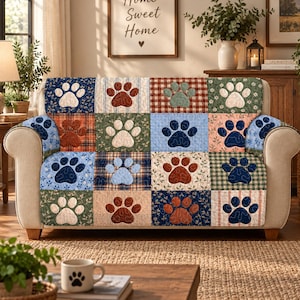 May include: A sofa cover featuring a patchwork design of various fabric squares, each displaying a single paw print. The patterns include plaid, floral, and solid textures in shades of blue, brown, green, and cream, with quilted stitching.