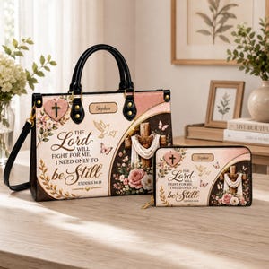 May include: A handbag and matching wallet set featuring a cream and brown floral design with a cross, butterflies, and the text The Lord will fight for me, I need only to be still, Exodus 14:14, and the name Sophia on a small rectangular plaque.
