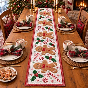 May include: A white quilted table runner featuring a repeating pattern of brown gingerbread people with red bow ties, green holly leaves, red berries, and red and white candy canes, bordered by a thin red line on a wooden dining table.