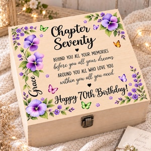 Puede incluir: Una caja de recuerdos cuadrada de madera con un cierre de metal, decorada con pensamientos morados, hojas verdes y mariposas coloridas. El texto dice: Chapter Seventy, BEHIND YOU ALL YOUR MEMORIES, before you all your dreams, AROUND YOU ALL WHO LOVE YOU, within you all you need, Grace, Happy 70th Birthday!
