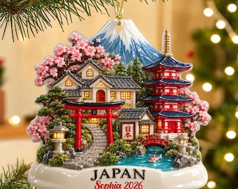 Op de afbeelding: Een decoratief ornament met een Japans landschap met de berg Fuji, een rode torii-poort, een pagode, kersenbloesems en een koivijver. De basis toont de tekst JAPAN en Sophia 2026 in zwarte en rode letters met een gouden ophangkoord.