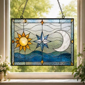 Peut inclure: Un panneau décoratif en vitrail rectangulaire représentant un soleil jaune, une étoile bleue et un croissant de lune blanc. Le motif inclut des lignes ondulées et une base bleu foncé, le tout dans un cadre en métal noir avec une chaîne de suspension.
