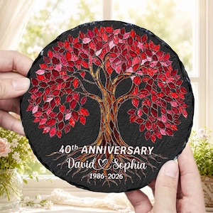 May include: A circular black slate plaque featuring a vibrant tree illustration with red and pink mosaic-style leaves. The text reads 40th ANNIVERSARY, David & Sophia, and 1986-2026. The tree trunk and roots are rendered in warm amber and brown tones.