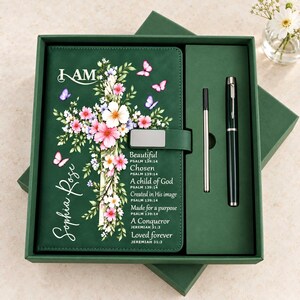 May include: A dark green journal with a floral cross graphic, butterflies, and the text I AM, Sophia Rose, and scripture verses. The journal includes a matching dark green pen and a refill cartridge, all presented in a dark green gift box.