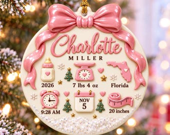 Op de afbeelding: Een rond crèmekleurig ornament met een roze strik aan de bovenkant en de naam Charlotte Miller. Het bevat iconen van een babyfles, weegschaal, kaart van Florida, klok, kalender met Nov 5 en meetlint met tekst 2026, 7 lbs 4 oz, Florida, 9:28 AM en 20 inches.