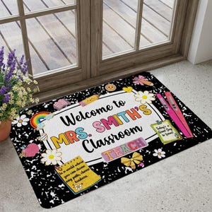Peut inclure: Un paillasson rectangulaire au fond noir et blanc moucheté avec le texte Welcome to MRS. SMITH'S CLASSROOM TEACH. Le motif comprend des illustrations colorées d'un arc-en-ciel, de fleurs, de crayons, d'un nœud et de notes adhésives.
