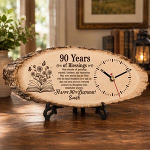 Könnte beinhalten: Eine Uhr aus einer Baumscheibe mit natürlicher Rinde, bedruckt mit einem offenen Buch, Blumen, Schmetterlingen, dem Text 90 Years of Blessings, einem Geburtstagswunsch und dem Namen Smith. Die Uhr hat schwarze Zeiger und einen roten Sekundenzeiger.