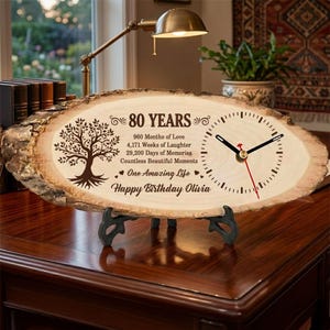 May include: A live edge wood slice clock featuring a laser-engraved tree, the text 80 YEARS, 960 Months of Love, 4,171 Weeks of Laughter, 29,200 Days of Memories, Countless Beautiful Moments, One Amazing Life, and Happy Birthday Olivia.