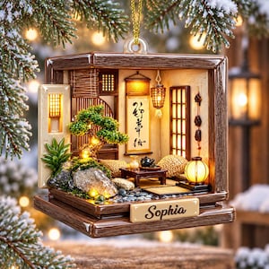 Könnte beinhalten: Ein quadratisches Ornament mit braunem Holzrahmen, das eine Miniatur-Innenszene mit einem Bonsai-Baum, einem Teeservice auf einem niedrigen Tisch, einer hängenden Schriftrolle mit schwarzer Kalligrafie und warmer Beleuchtung zeigt. Der Name Sophia steht auf einer Plakette.
