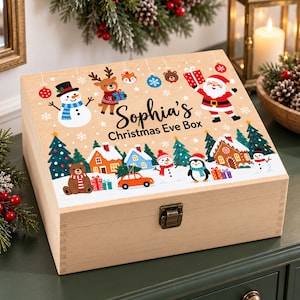 May include: A rectangular wooden box with a metal latch, featuring a printed Christmas scene with a snowman, reindeer, Santa Claus, a gingerbread house, and the text Sophia's Christmas Eve Box. The design includes colourful holiday icons.