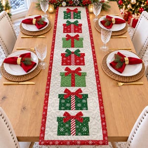 May include: A rectangular table runner featuring a cream-colored background with a repeating pattern of red and green gift boxes adorned with bows. The runner has a red border with white snowflake details and is placed on a wooden dining table.