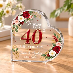 Könnte beinhalten: Eine herzförmige, transparente Acrylplatte mit einem Blumenmuster aus roten und weißen Rosen, grünen Blättern und goldenen Akzenten. Der Text lautet Happy 40th ANNIVERSARY, Jame & Sophia und 1986 2026. Die Zahl 40 ist in großem Rot und Gold dargestellt.