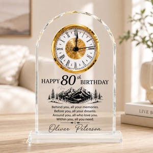 May include: An arched clear glass desk clock with a gold-rimmed face, Roman numerals, and black hands. It features the text "HAPPY 80th BIRTHDAY," a mountain landscape graphic, the quote "Behind you, all your memories," and the name "Oliver Peterson."