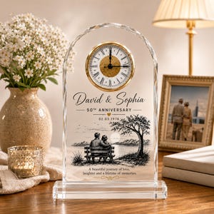 May include: An arched glass clock featuring a gold-rimmed face with Roman numerals. The glass is etched with the names David & Sophia, 50th Anniversary, the date 02.03.1976, a graphic of a couple on a bench under a tree, and the text A beautiful journey of love, laughter and a lifetime of memories.