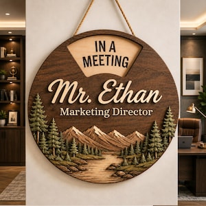 May include: A circular wooden sign featuring a landscape of mountains, a river, and pine trees. The text reads IN A MEETING, Mr. Ethan, and Marketing Director. The sign is dark brown with lighter wood accents and hangs from a rope.