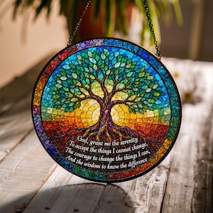 May include: A circular stained glass suncatcher featuring a tree with green leaves and brown roots. The background transitions from blue at the top to yellow and red at the bottom. The text reads: God, grant me the serenity to accept the things I cannot change, the courage to change the things I can, and the wisdom to know the difference.