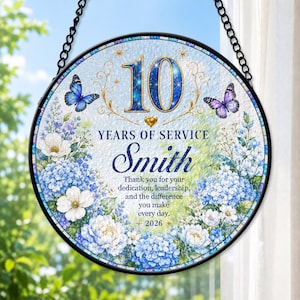 May include: A circular hanging plaque with a black frame and chain, featuring a blue and white floral design with two butterflies. Text reads: 10 YEARS OF SERVICE Smith Thank you for your dedication, leadership, and the difference you make every day. 2026.