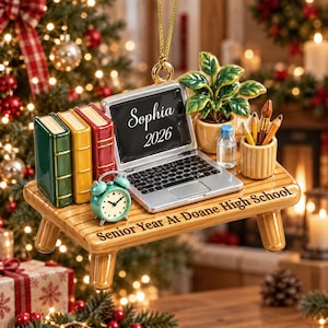 May include: A ceramic ornament featuring a desk with a laptop displaying "Sophia 2026", three books, a green alarm clock, a potted plant, a water bottle, and a pencil holder. The desk is inscribed with "Senior Year At Doane High School".