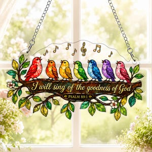 Puede incluir: Un adorno colgante estilo vitral con siete pájaros coloridos posados en una rama. Los pájaros son rojos, naranjas, amarillos, verdes, azules, morados y rosas. El texto dice I will sing of the goodness of God y PSALM 89:1.