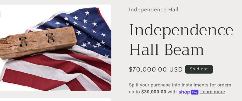 May include: A weathered wooden beam with two carved openings rests atop a folded American flag. The flag displays red and white stripes and a blue field with white stars. The text "Independence Hall Beam" is visible.