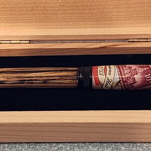 May include: A wooden pen with a striped pattern and a stamp-themed design, presented in a light-colored wooden box with a black velvet interior. The pen features the text "Providence Hall 1753" and "10&cent;".