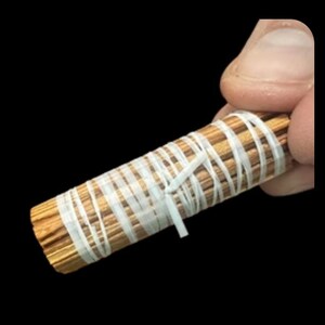 May include: A bundle of thin, light brown sticks wrapped with white tape. The sticks are tightly bound together, forming a cylindrical shape. The white tape is wrapped around the bundle in a crisscross pattern.