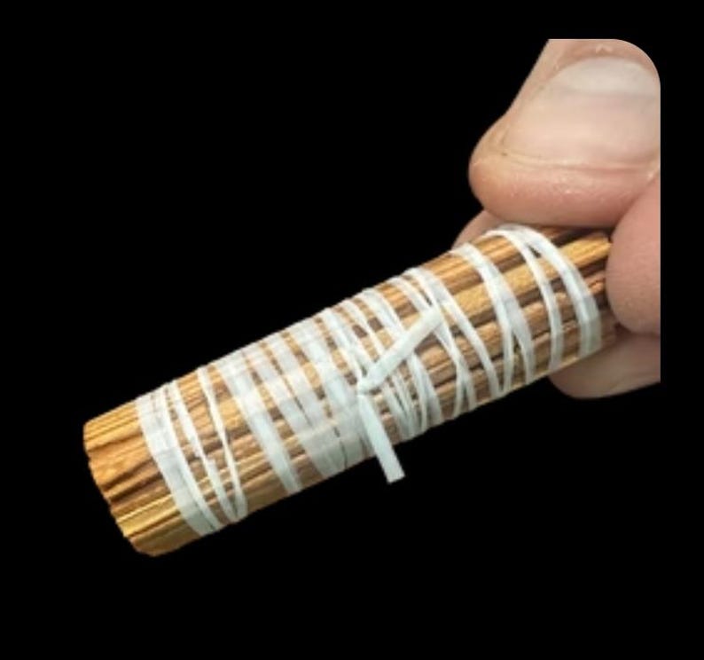 May include: A bundle of thin, light brown sticks wrapped with white tape. The sticks are tightly bound together, forming a cylindrical shape. The white tape is wrapped around the bundle in a crisscross pattern.
