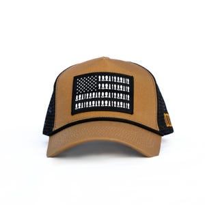 May include: A tan baseball cap with a black mesh back and a black rectangular patch on the front. The patch features a white graphic design of the American flag where the stars and stripes are replaced by silhouettes of various ammunition rounds.