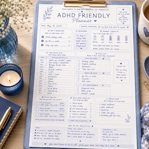 May include: A blue ADHD-friendly planner on a clipboard with a floral design, a lit candle, a mug with a heart, and a notebook with the text "small steps, big future". The planner includes sections for priorities, time blocks, and self-care.