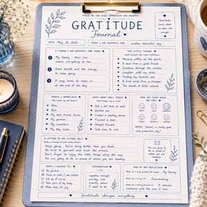 May include: A blue clipboard with a "Gratitude Journal" design, featuring handwritten prompts and a gold clip. Includes a notebook, pen, candle, and a cup of coffee. The journal encourages reflection and appreciation.