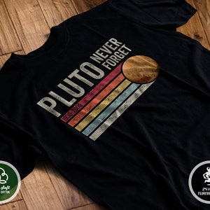 May include: Black t-shirt with a vintage-style graphic that says "Pluto Never Forget 1930-2006" with a stylized image of Pluto in the upper right corner.