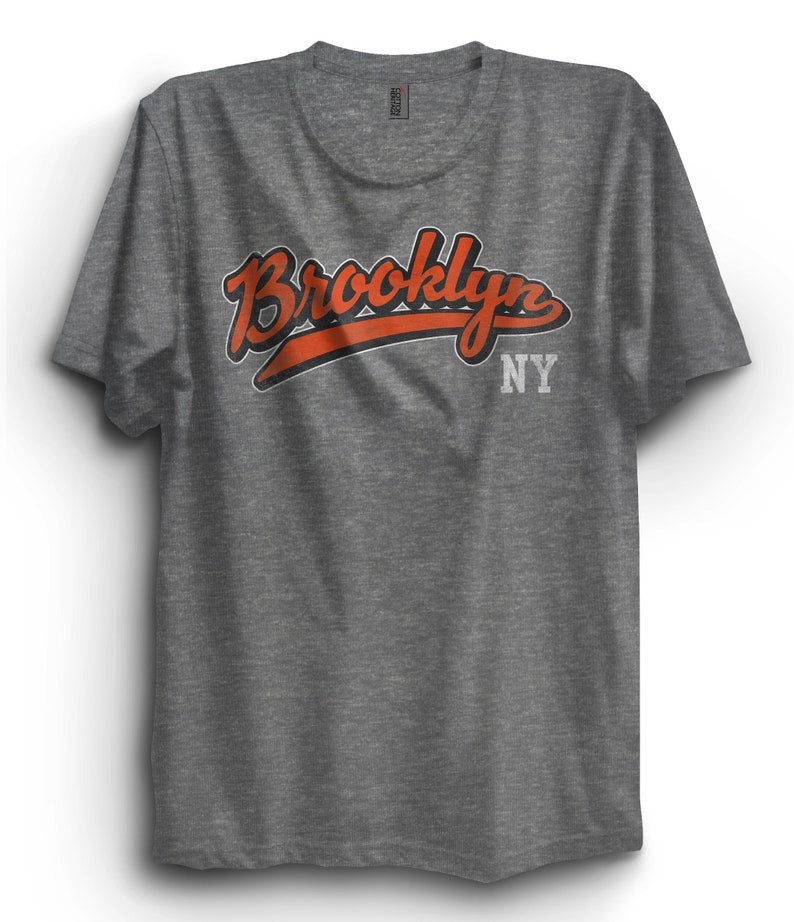 May include: A heather grey t-shirt with a red and black graphic that says "Brooklyn NY" in a vintage style font.
