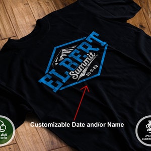May include: Black t-shirt with a blue and white graphic design of a mountain range with the text "ELBERT Summit 10-6-22". The design is in a hexagon shape.