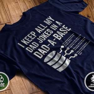 May include: A navy blue t-shirt with a white graphic design of a database icon and the text "I keep all my dad jokes in a dad-a-base".