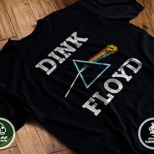 May include: Black t-shirt with a white graphic of a triangle with a rainbow beam and a yellow disc. The text "DINK FLOYD" is printed in white on the shirt.