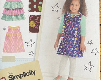May include: A girl in a blue floral dress with a rainbow collar and straps. The image includes a pink polka dot dress, a tiered dress, and fabric swatches. The Simplicity logo is also visible.