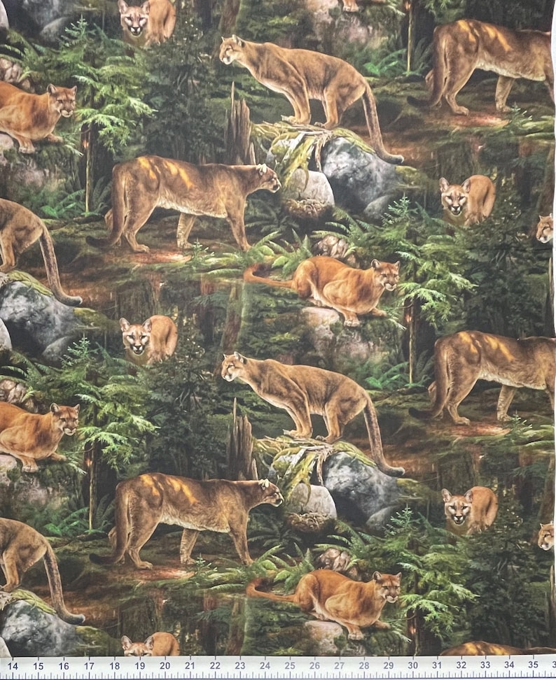 May include: A fabric featuring a repeating pattern of cougars in a forest environment. The cougars are depicted in shades of brown and tan, set against a backdrop of green foliage, rocks, and trees. The image has a realistic, detailed style.