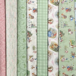 May include: A collection of eight vertical fabric strips featuring various patterns including Peter Rabbit illustrations, soft pink floral motifs, light green botanical designs, and a green plaid print, displayed side by side in a continuous row.