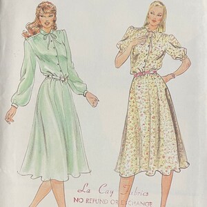 May include: Two women's dresses with long sleeves and a bow at the neck. The dress on the left is a solid green color and the dress on the right is a floral print with a yellow background. The text "La Cay Fabrics" and "NO REFUND OR EXCHANGE" is at the bottom of the image.