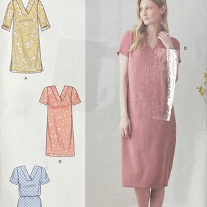 May include: Simplicity sewing pattern S9262 for a V-neck dress with short sleeves. The envelope displays three illustrated variations: a yellow floral print, a peach patterned design, and a blue geometric print, alongside a photo of a solid mauve dress.