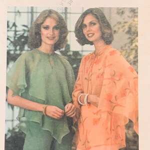 May include: Two women wearing sheer tops with long sleeves and a flowing design. The woman on the left is wearing a green top and the woman on the right is wearing a peach top with a floral pattern.