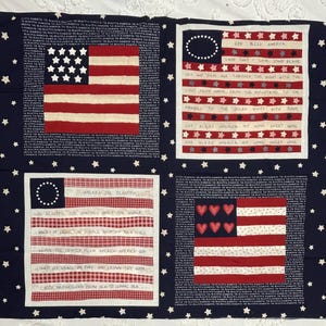 May include: A navy blue fabric panel featuring four distinct rectangular blocks with American flag motifs, white stars, and printed lyrics from God Bless America and America the Beautiful. The borders contain repeating text and small patriotic icons.