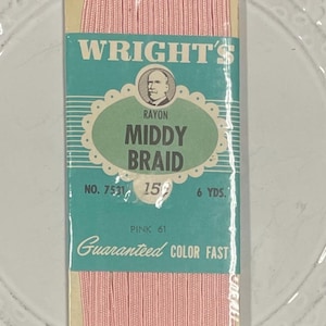 May include: A packet of Wright's rayon Middy Braid in pink. The label is teal with a portrait and text that reads "Guaranteed Colour Fast". The packet contains 5.49 metres of braid.