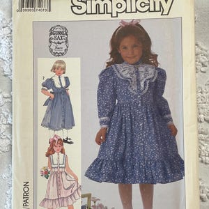May include: Simplicity sewing pattern for a Gunne Sax dress, size 6. The pattern features illustrations of girls' dresses, including a blue floral dress with a white lace collar and cuffs. The pattern's cover is aged.