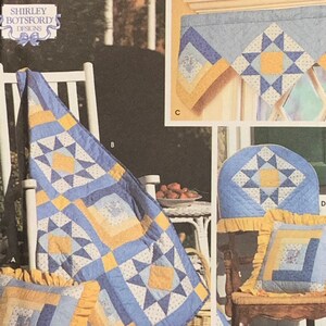 May include: A collection of quilted home decor items in shades of blue, yellow, and white. The items include a quilt draped over a rocking chair, a pillow, a chair cover, and a window valance. The designs feature star and square patterns.